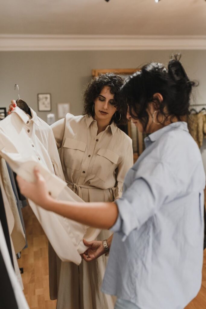 Two women shopping and discussing clothes in a stylish boutique, focusing on a beige shirt.